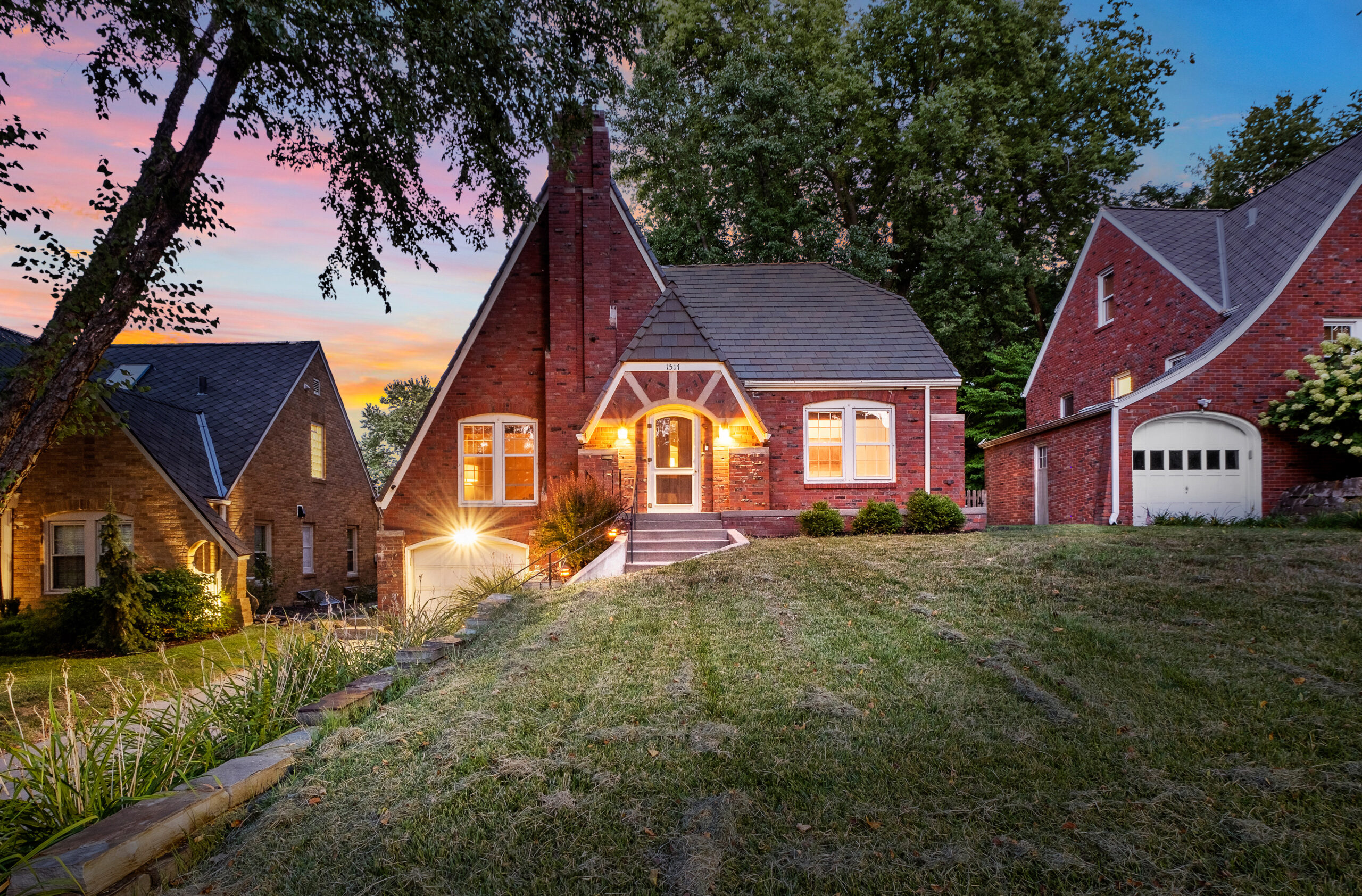 Red tudor brick house with porch lights at twilight