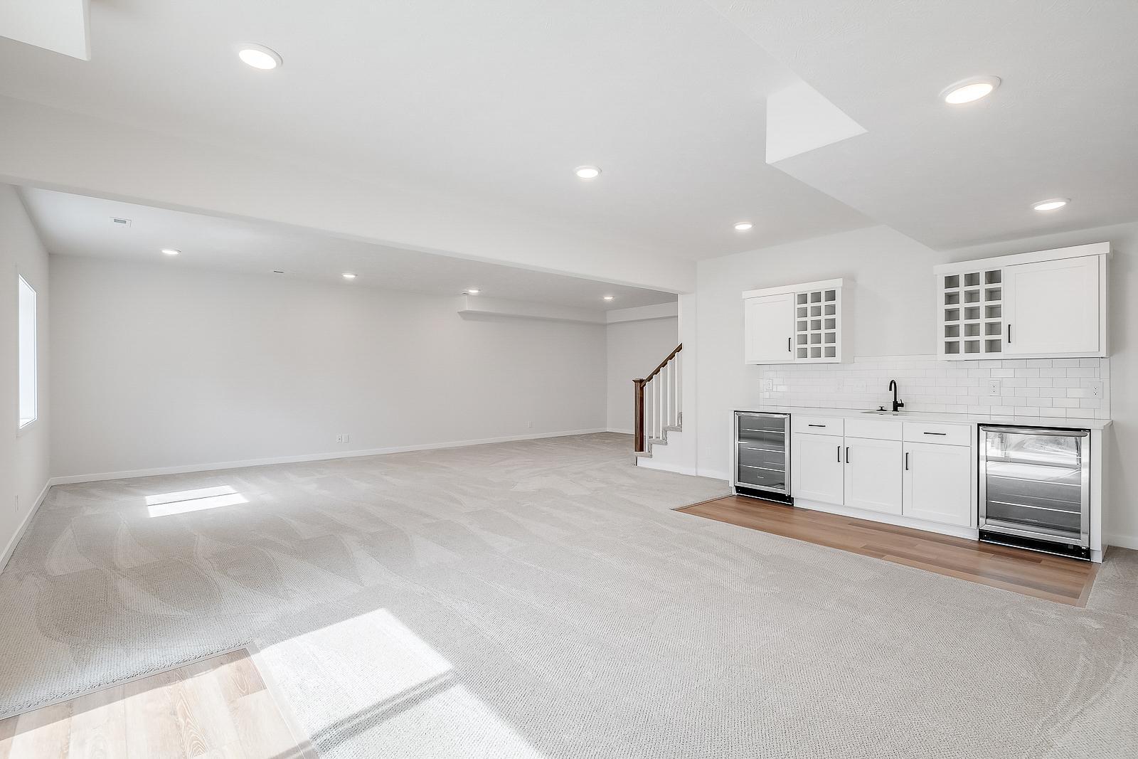 Finished and carpeted downstairs basement with bar area including sink, cabinets, and wine fridges.