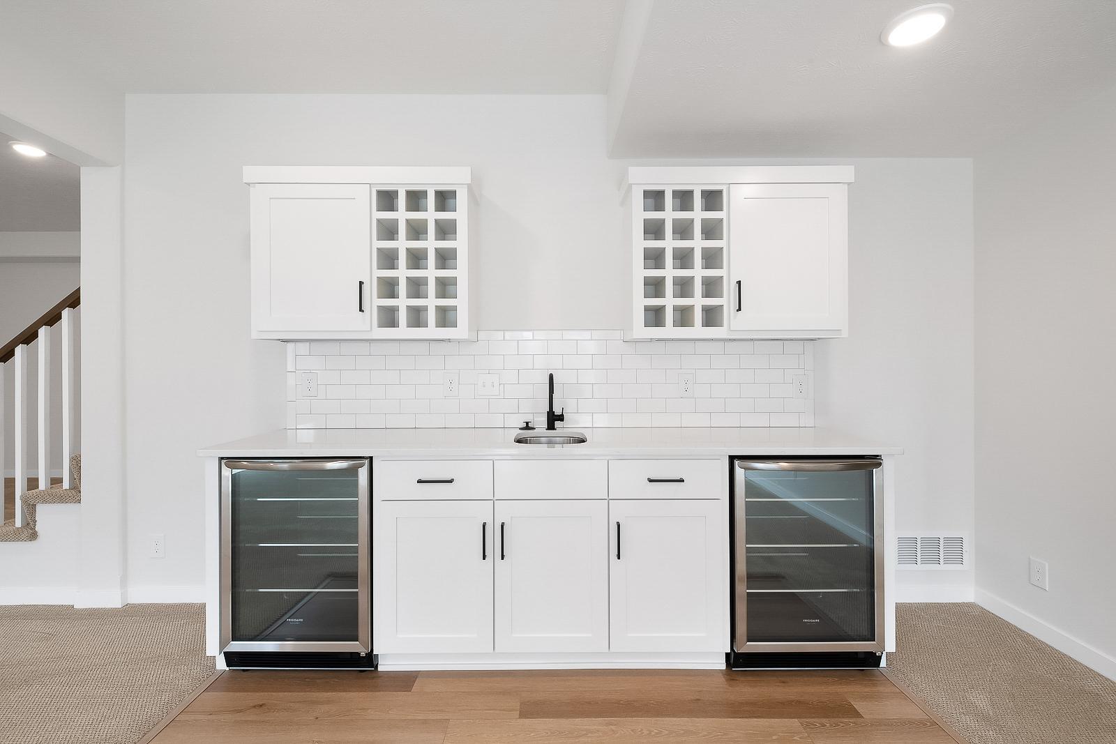 Close up of bar area with wine fridges, sink, and cabinets.