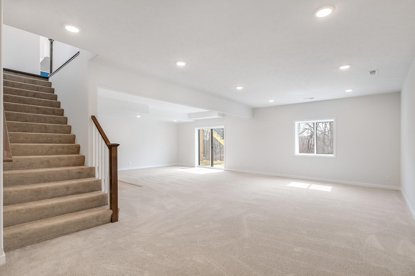 Finished basement with stairs from ground level and sliding doors leading to cement base of exterior backyard deck.