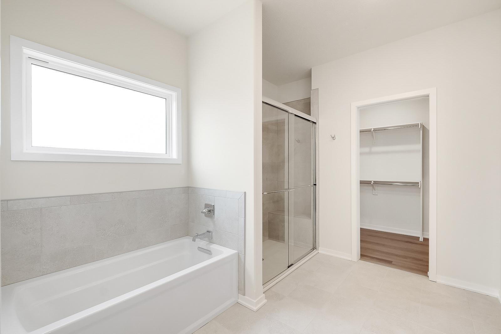 Bathroom attached to walk-in closet with stand-up shower and detached tub underneath long frosted window.