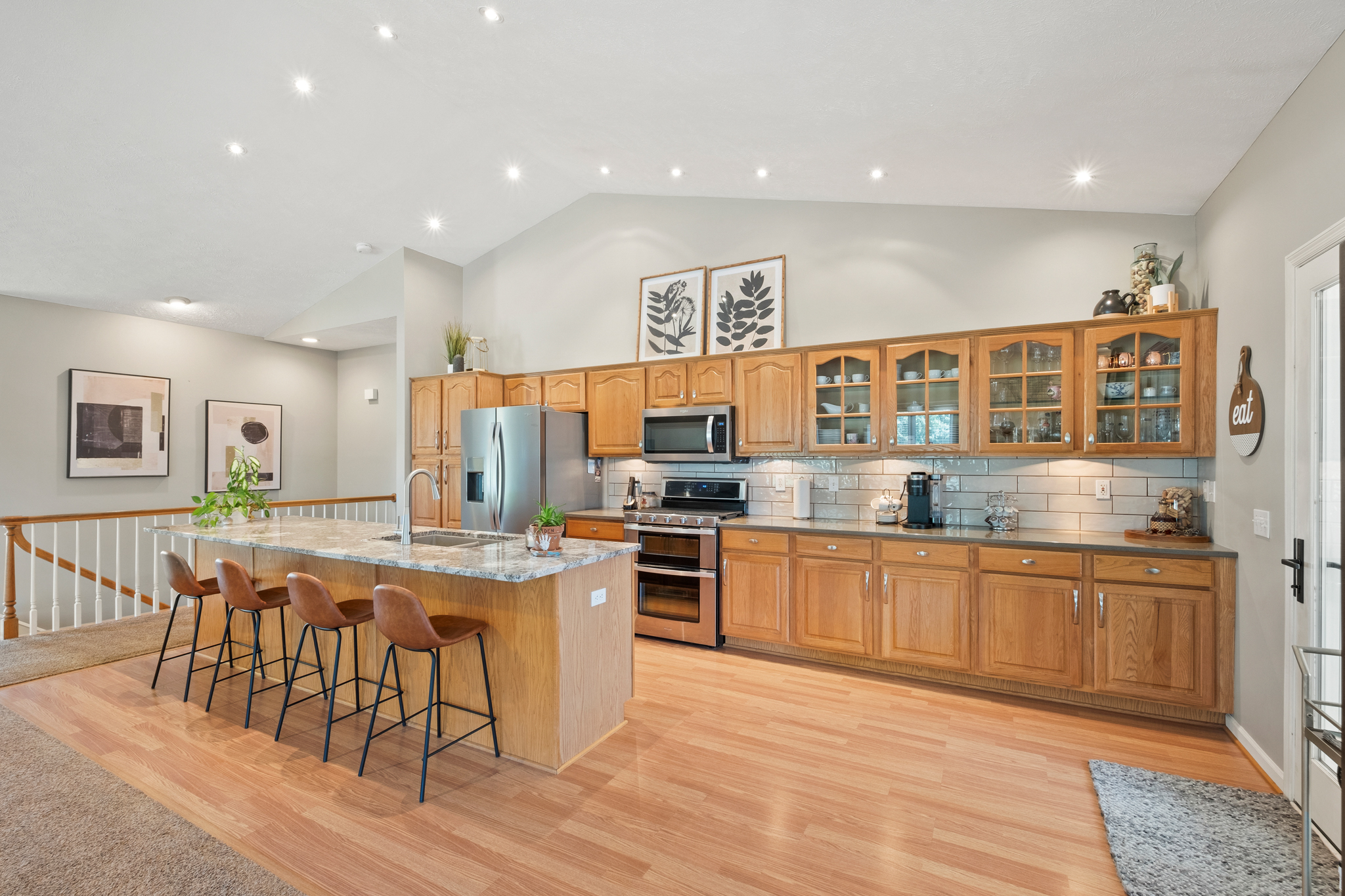 A white walled, high-ceiling kitchen with wooden cabinets and flooring and an island.