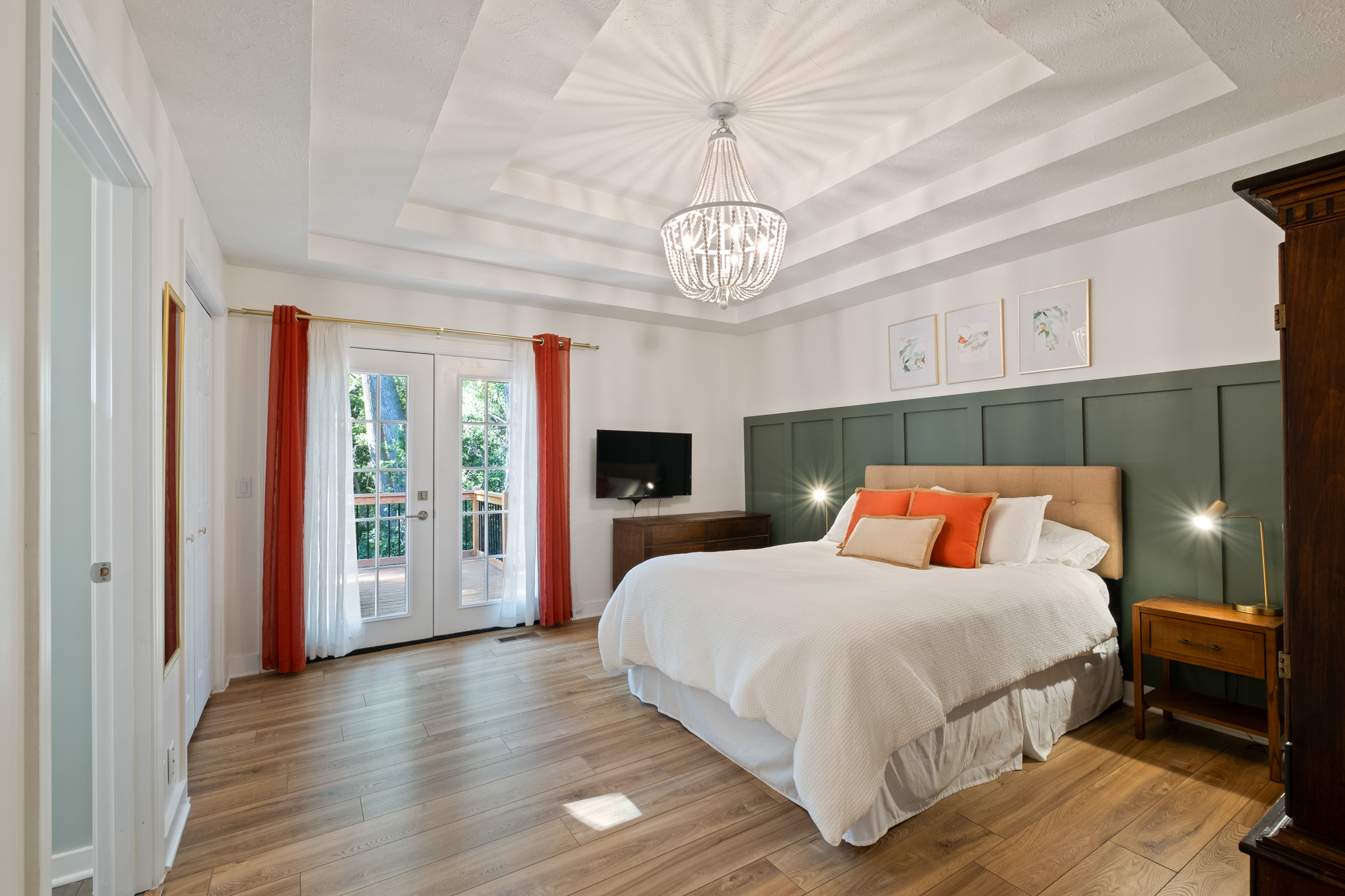 A master bedroom with wood flooring, sage green accent wall, and orange and white bedding.