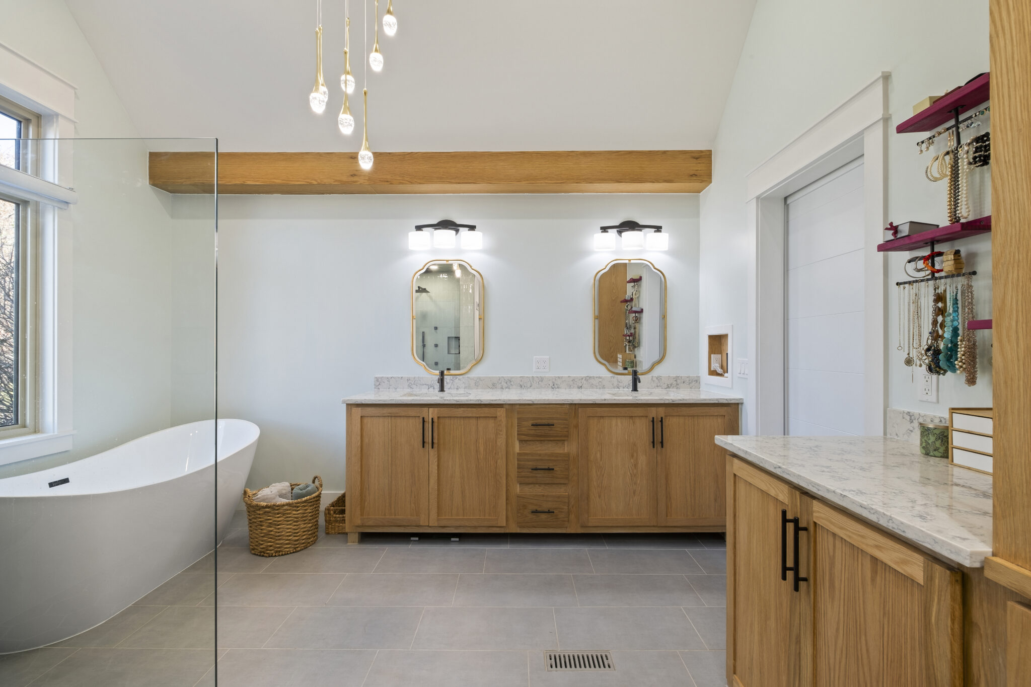 A grey and white bathroom with light wood accent beam and cabinets.