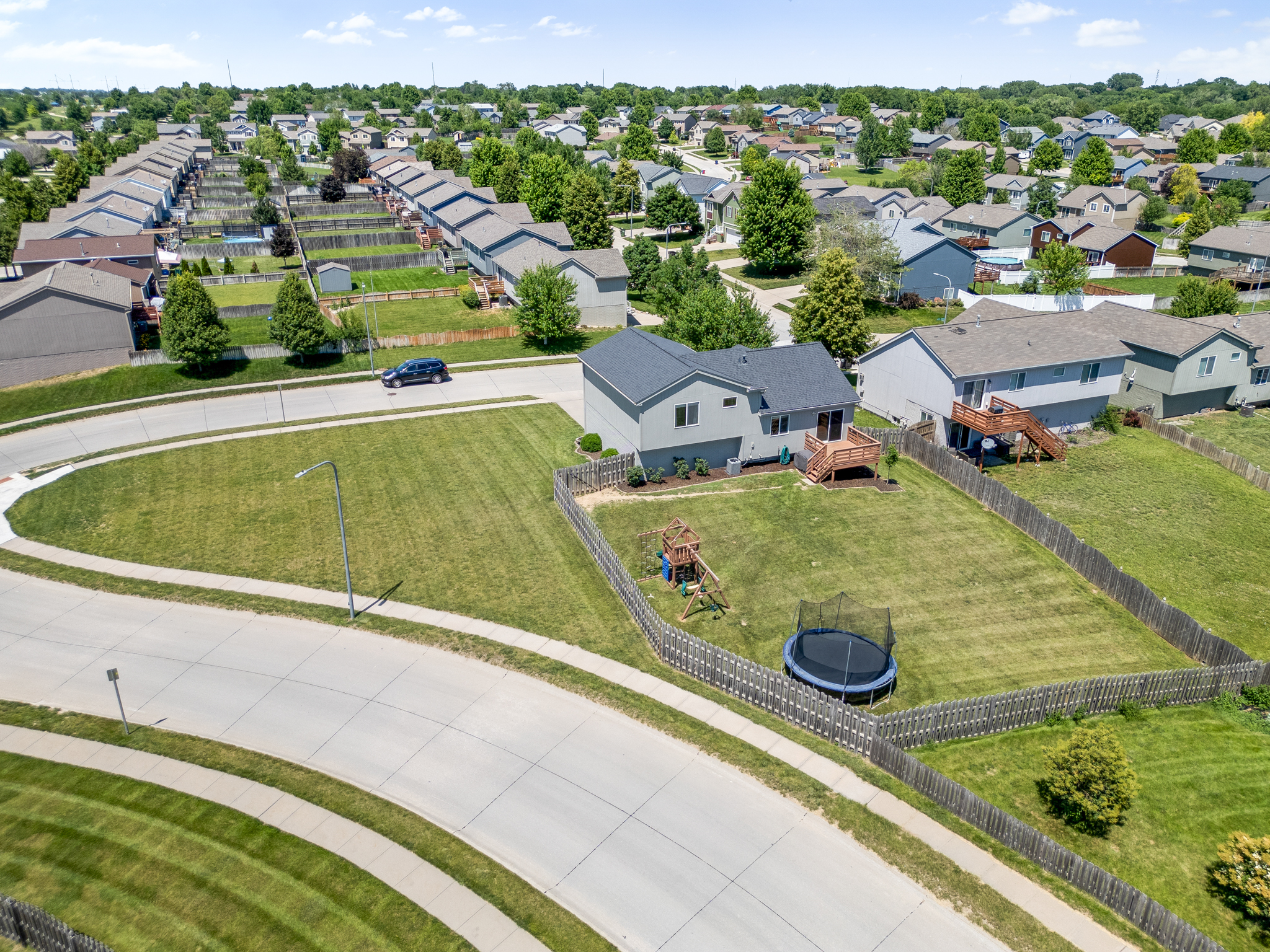 Aerial drone image of a home with a fenced backyard, wooden deck, and oddly shaped side property.