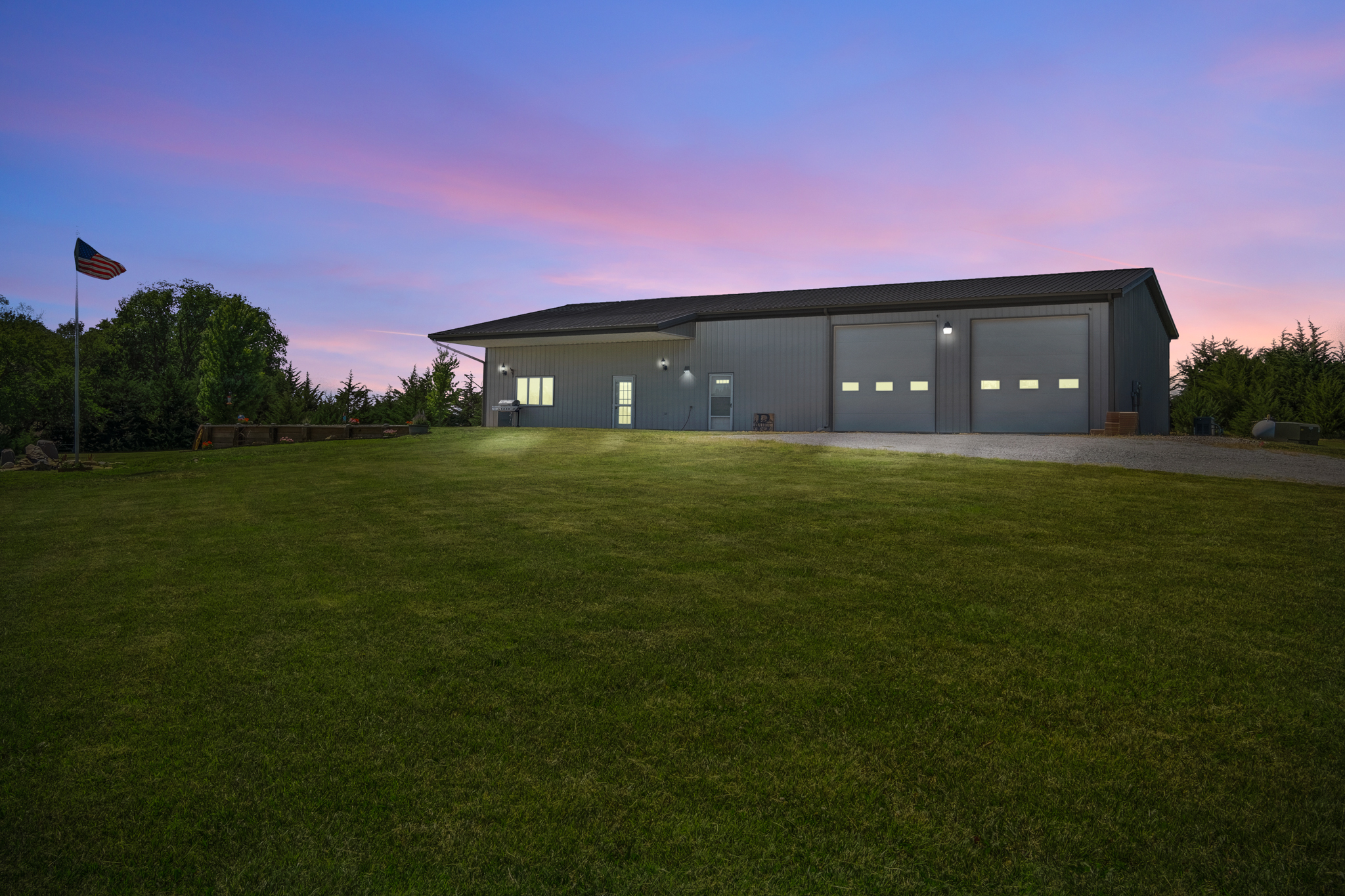 Grey barn at sunset, with green lawn, and American flag.